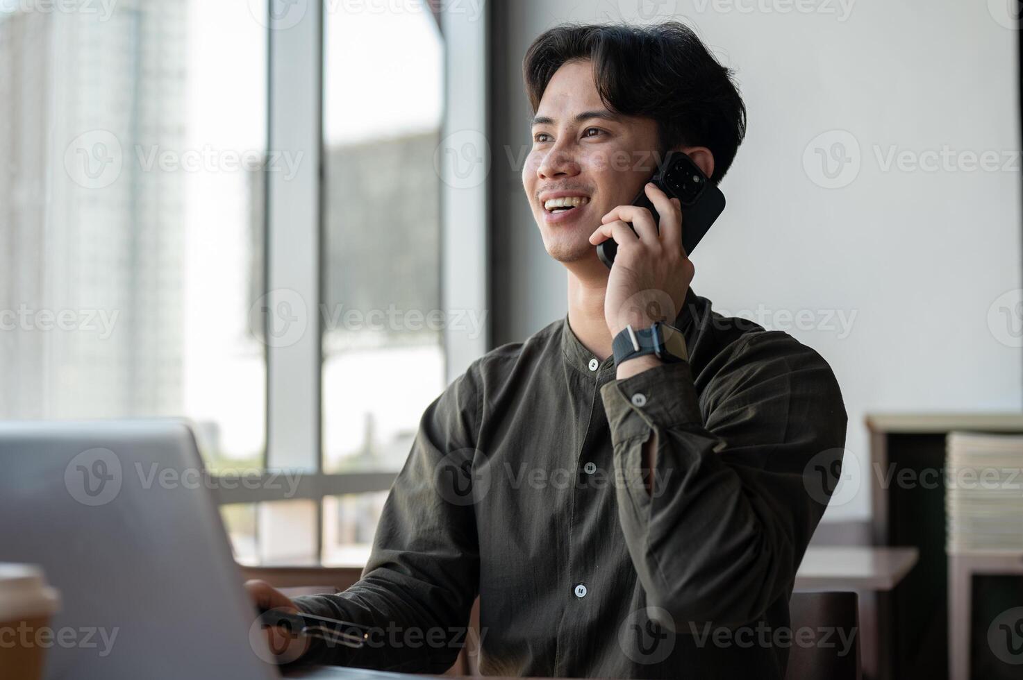 A positive Asian businessman talking on the phone while working remotely from a coffee shop. photo