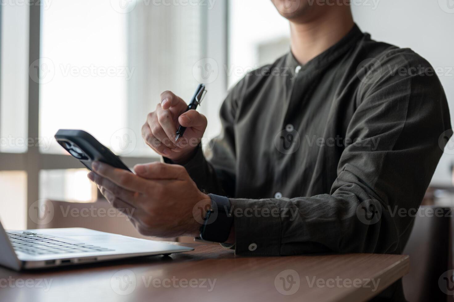 A close-up of an Asian businessman using his smartphone while working in a modern office. photo