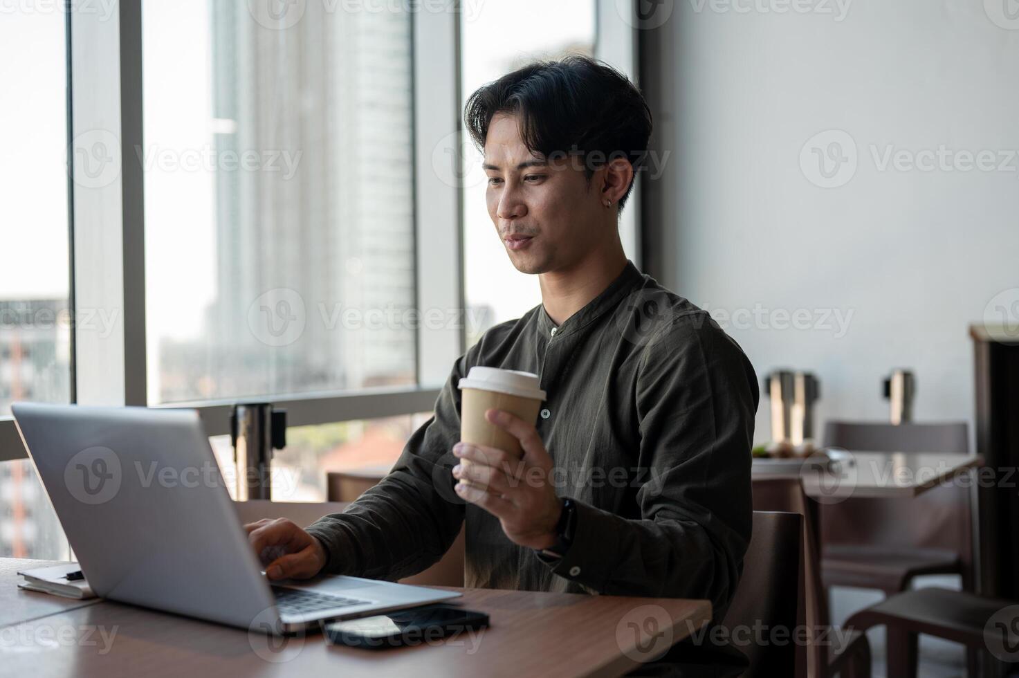 A positive Asian businessman enjoying a hot drink while working on his laptop, working remotely. photo