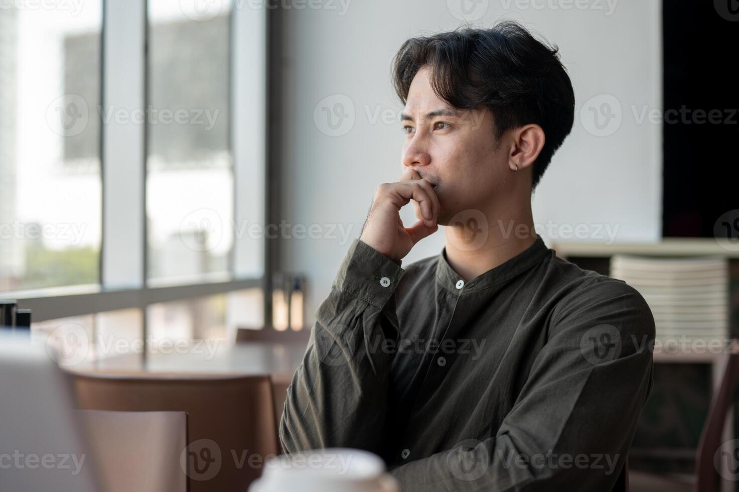 A thoughtful Asian businessman admiring the view outside with a serious expression while working. photo