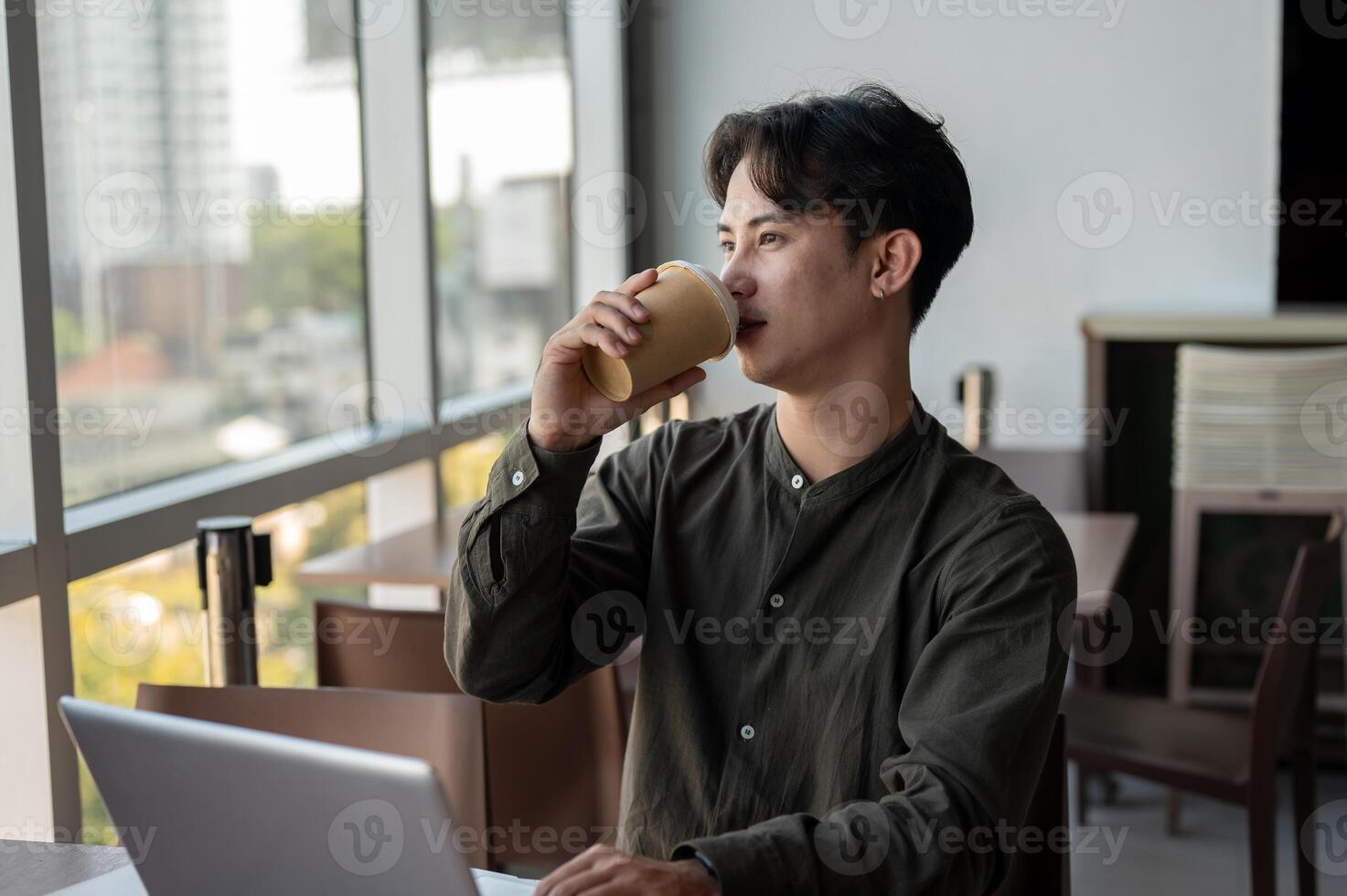 A positive Asian businessman enjoying a hot drink while working on his laptop, working remotely. photo