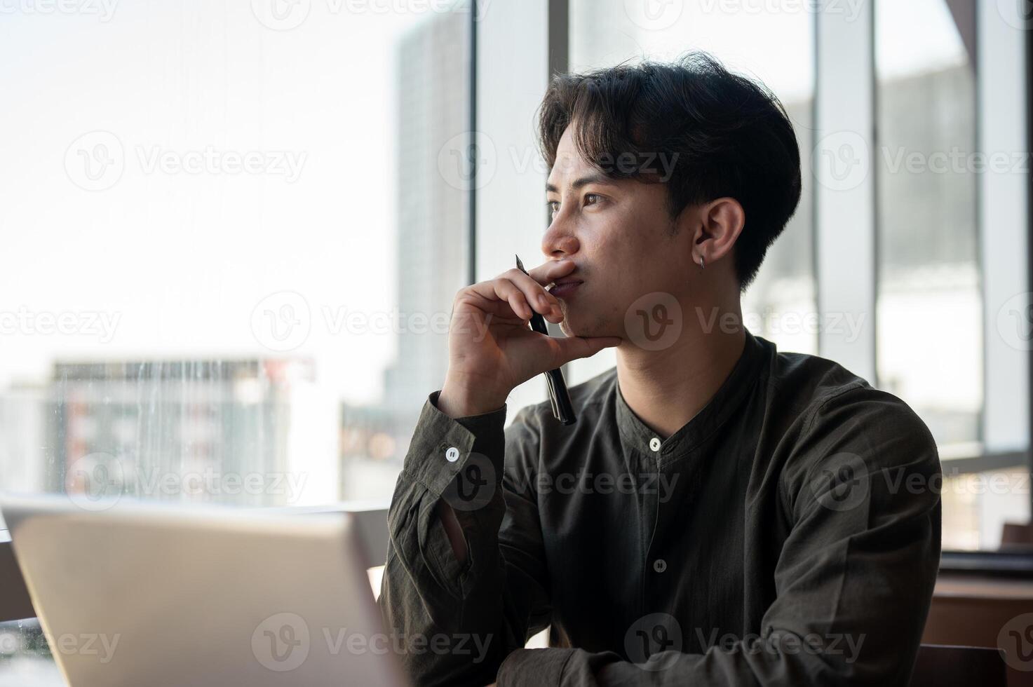 A thoughtful Asian businessman admiring the view outside with a serious expression while working. photo