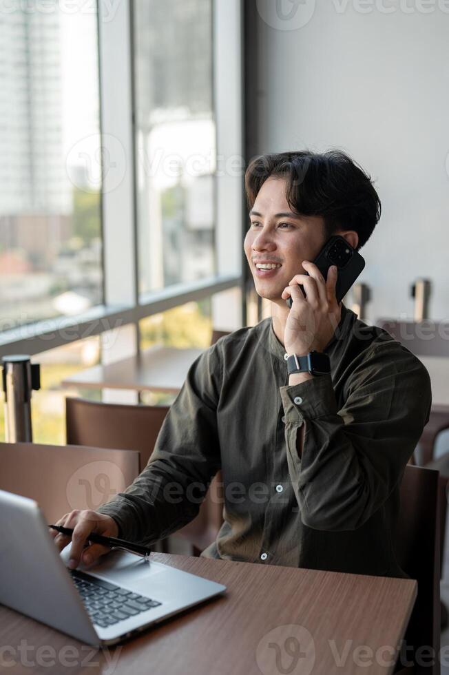 A positive Asian businessman talking on the phone while working remotely from a coffee shop. photo