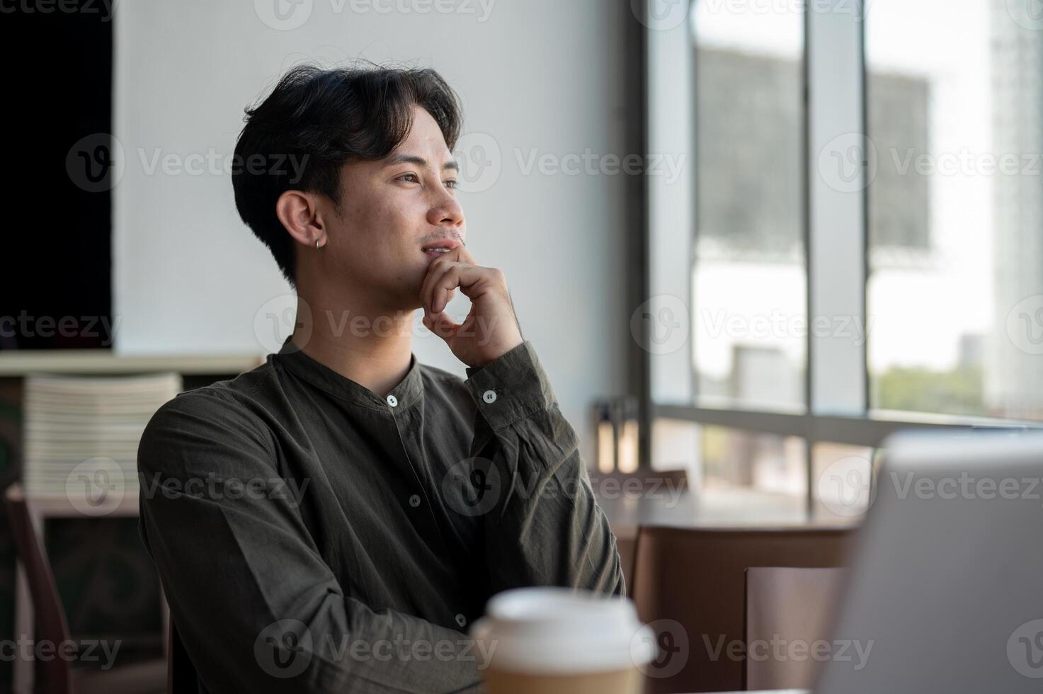 A positive Asian businessman looking out the window while sitting at a table in a coffee shop. photo