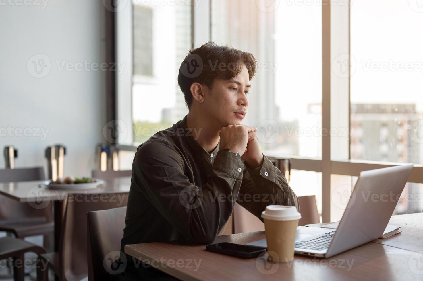 A thoughtful, serious Asian businessman reading an email on his laptop with a serious expression. photo