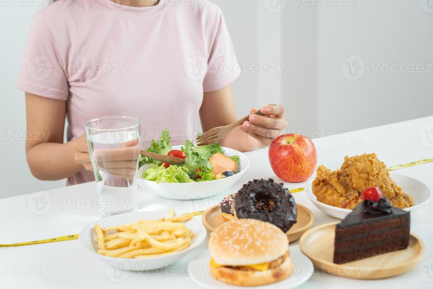 Woman choose healthy food for diet. Healthy food and fatty food separated on table with measuring tape. Lose weight, balance, control, reduce fat, low calorie, routine, exercise, body shape. photo