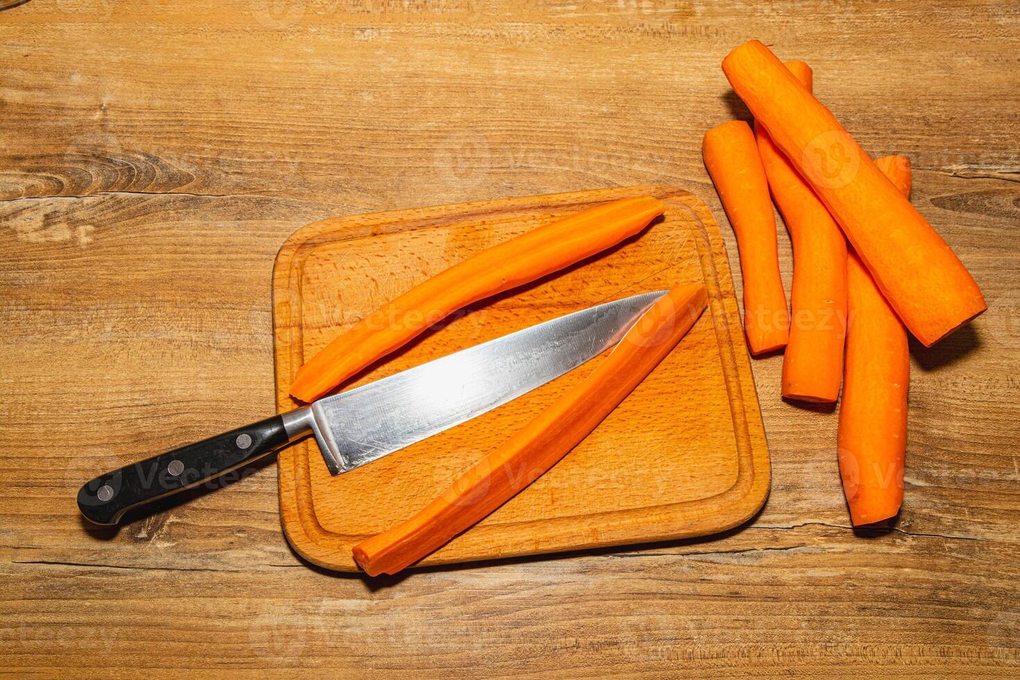 Carrots cut into pieces on a kitchen board, next to a knife photo