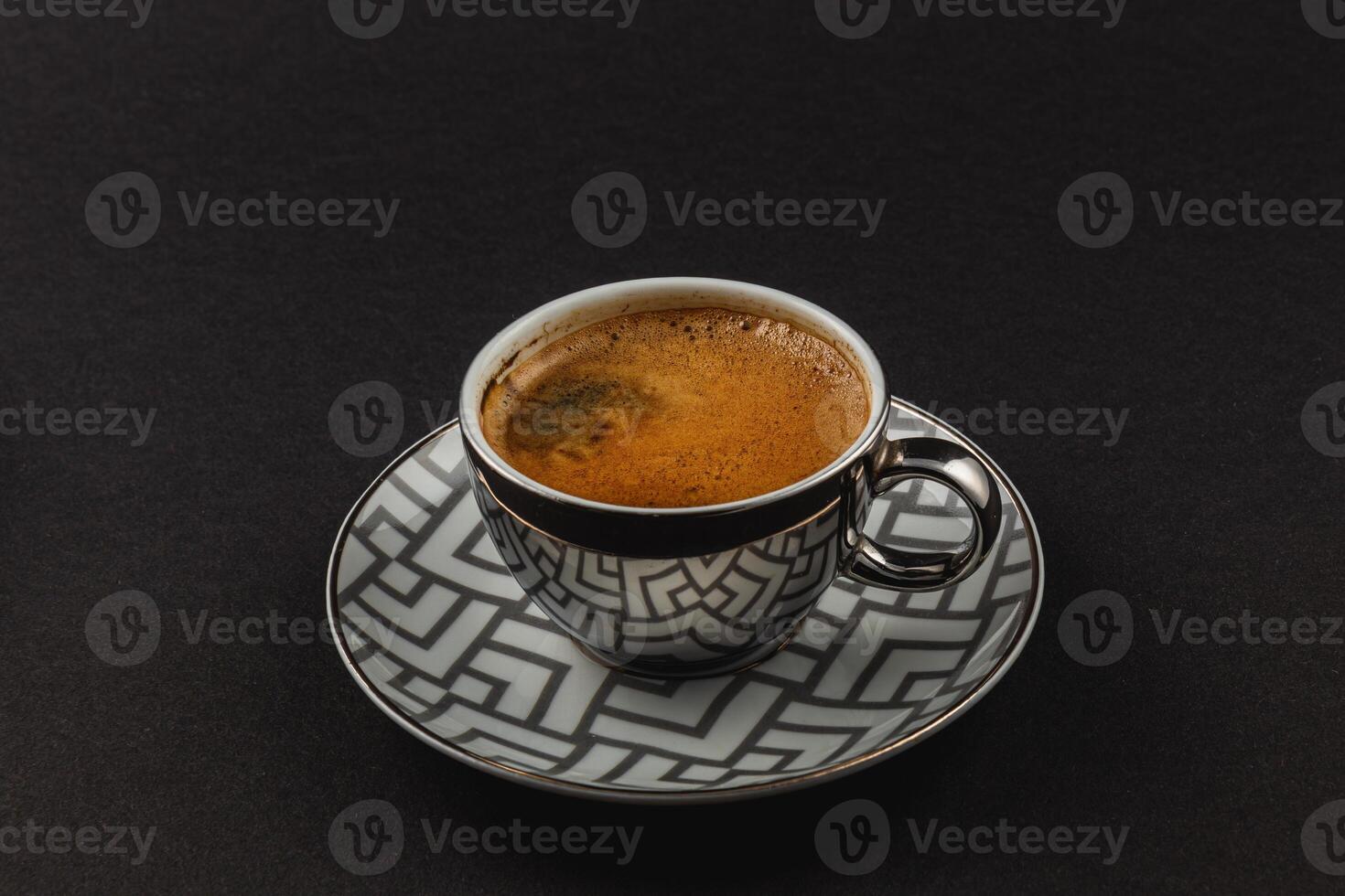 Fresh strong espresso in a silver cup on a plate on a black background photo