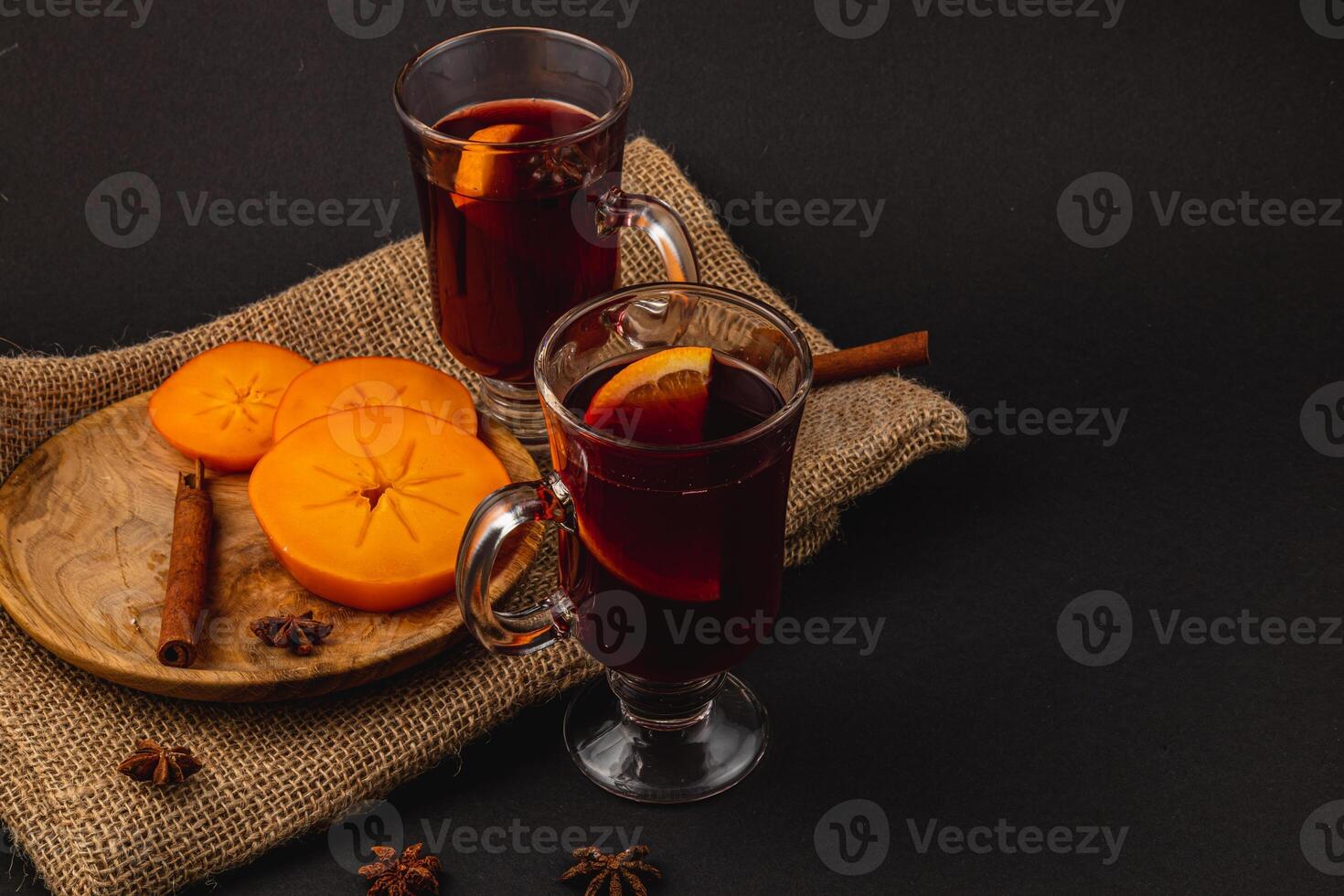 Delicious mulled wine with spices and sweet persimmons on a wooden plate photo