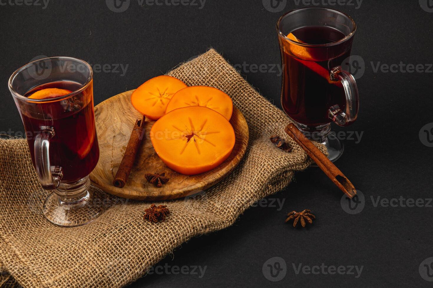 Delicious mulled wine with spices and sweet persimmons on a wooden plate photo