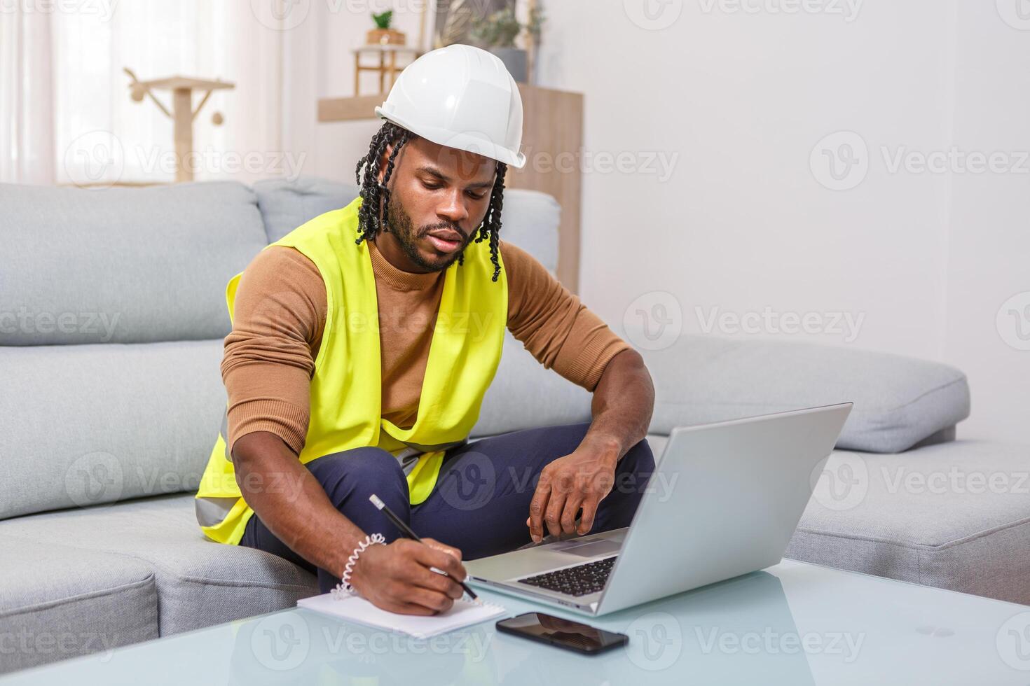 Construction worker reviews blueprints while working from home on a laptop during the morning photo