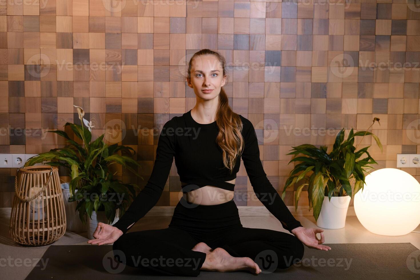 An athletic girl in black sportswear sits in lotus pose at a yoga class in a fitness room among green indoor plants photo