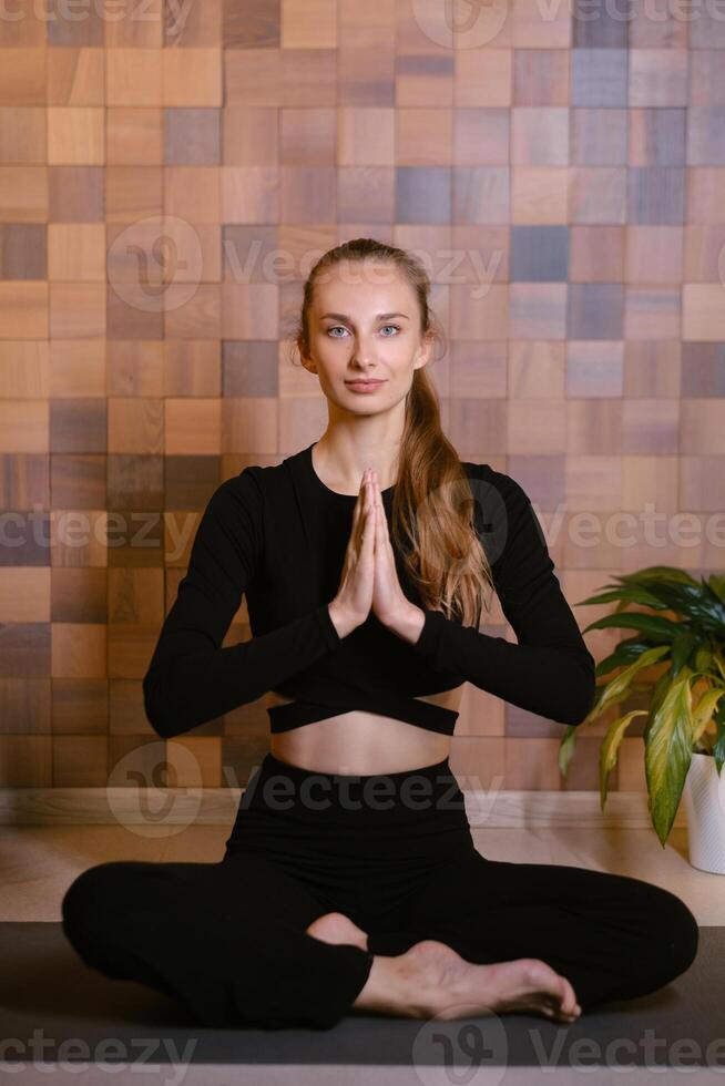 An athletic girl in black sportswear sits in lotus pose at a yoga class in a fitness room among green indoor plants photo