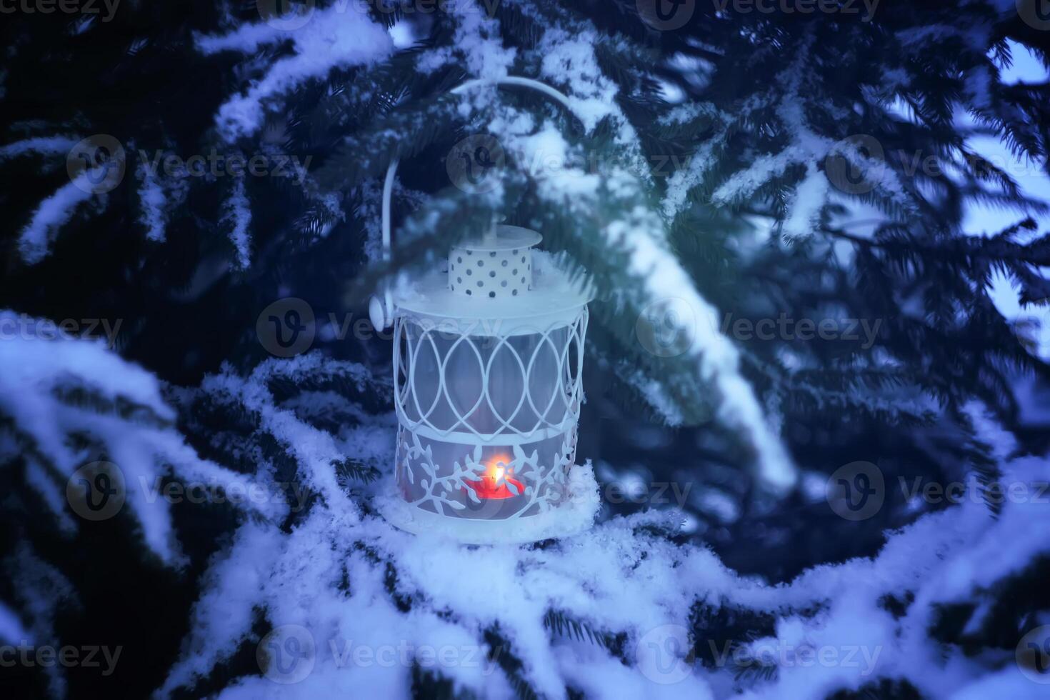 Decorative Christmas lantern with burning candle hanging on snow-covered fir- tree branch in a winter park. New year festive card, poster, postcard design. photo