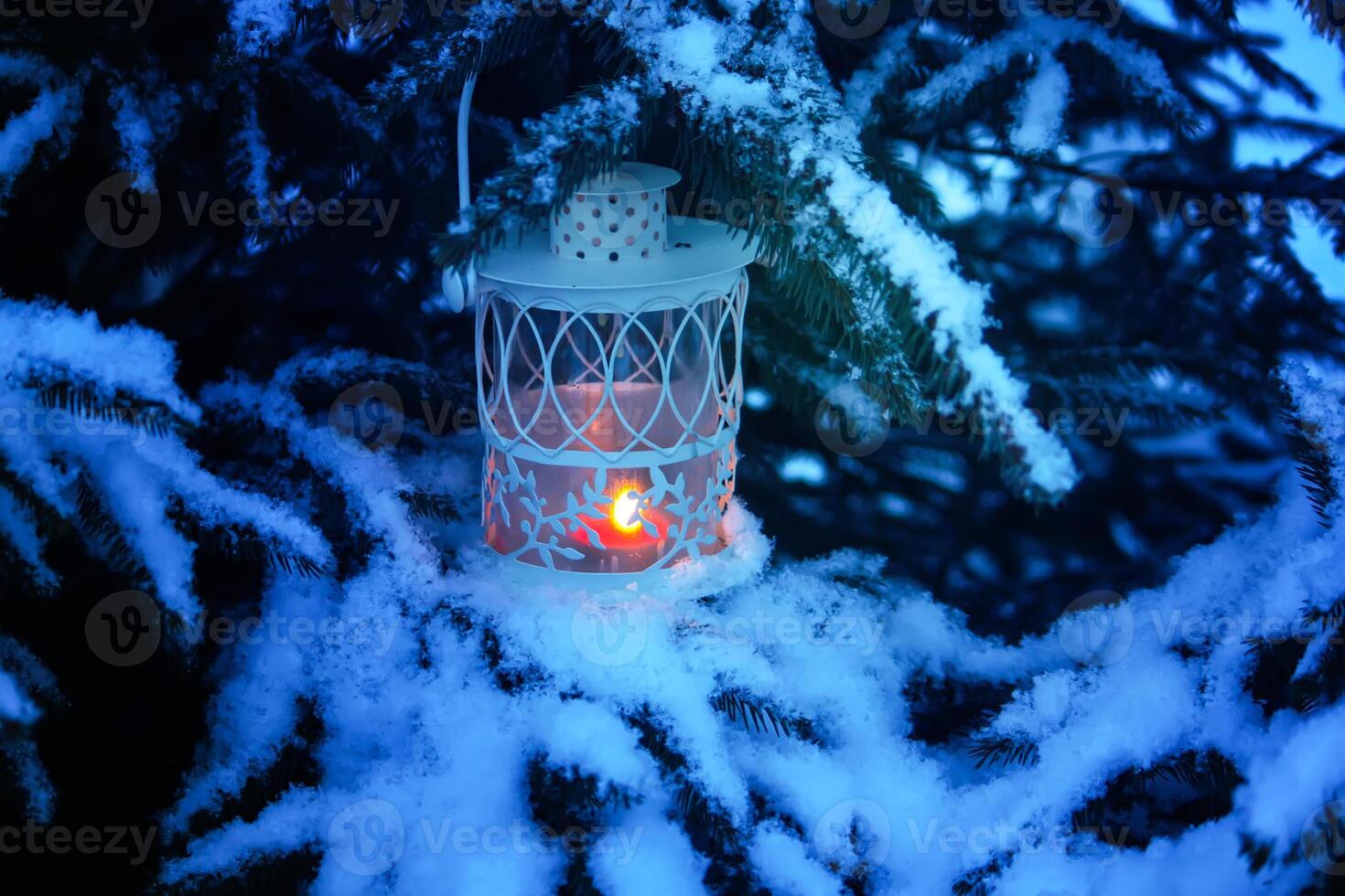 Decorative Christmas lantern with burning candle hanging on snow-covered fir- tree branch in a winter park. New year festive card, poster, postcard design. photo