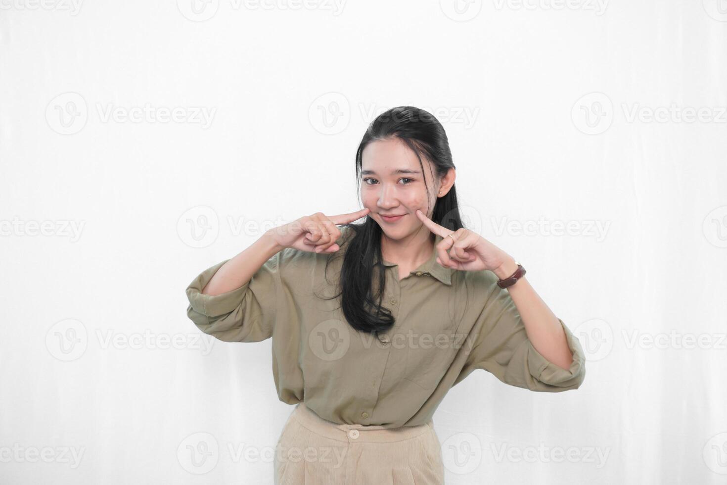The smiling expression of an Indonesian Asian woman in green and touching her cheek with her finger photo