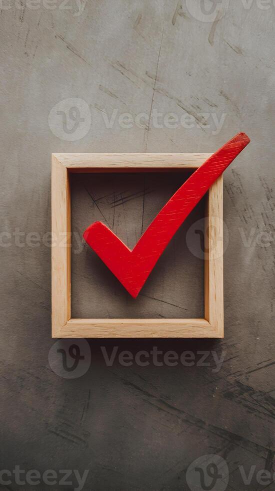 A red checkmark rests in a clean wooden frame on a textured surface Vertical Mobile Wallpaper photo