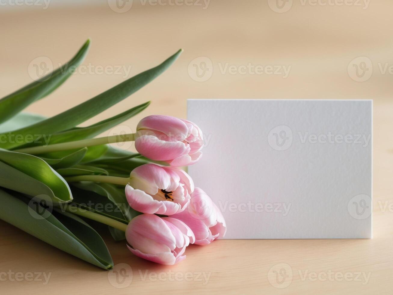 Fresh pink tulips and a blank white card on a light wooden background ideal for greeting messages or invitations. photo