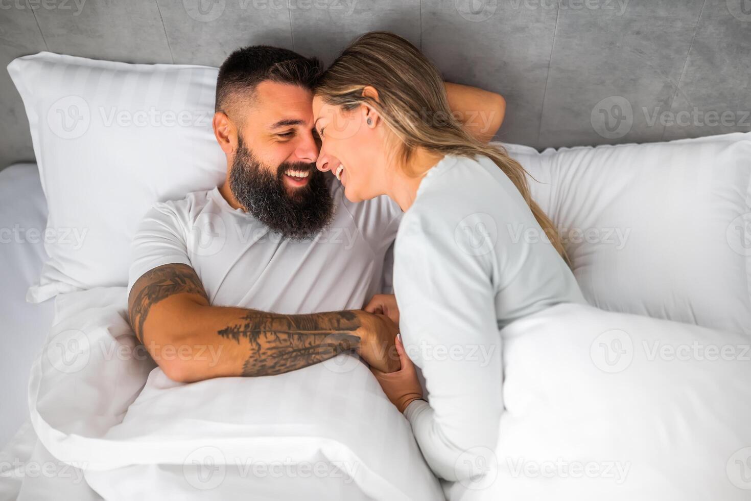 Young happy loving couple is lying in bed in the morning. They are relaxing and smiling. photo