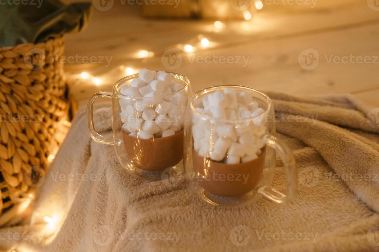 Two glass mugs of hot chocolate with marshmallows on cozy blanket. photo
