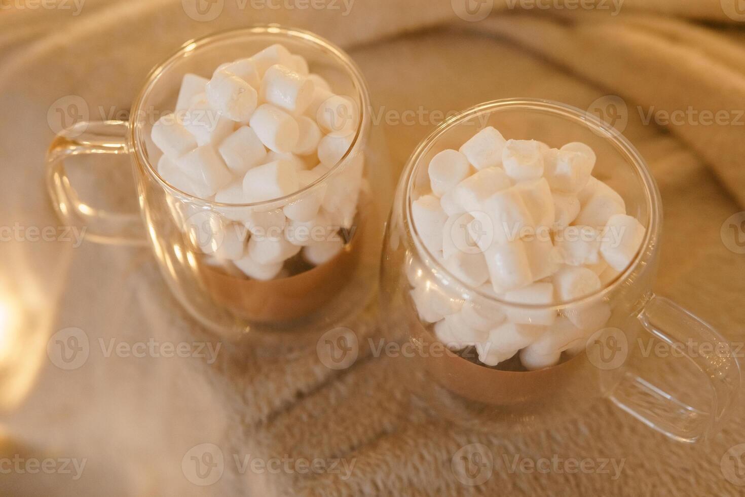 Two glass mugs of hot chocolate with marshmallows on cozy blanket. photo