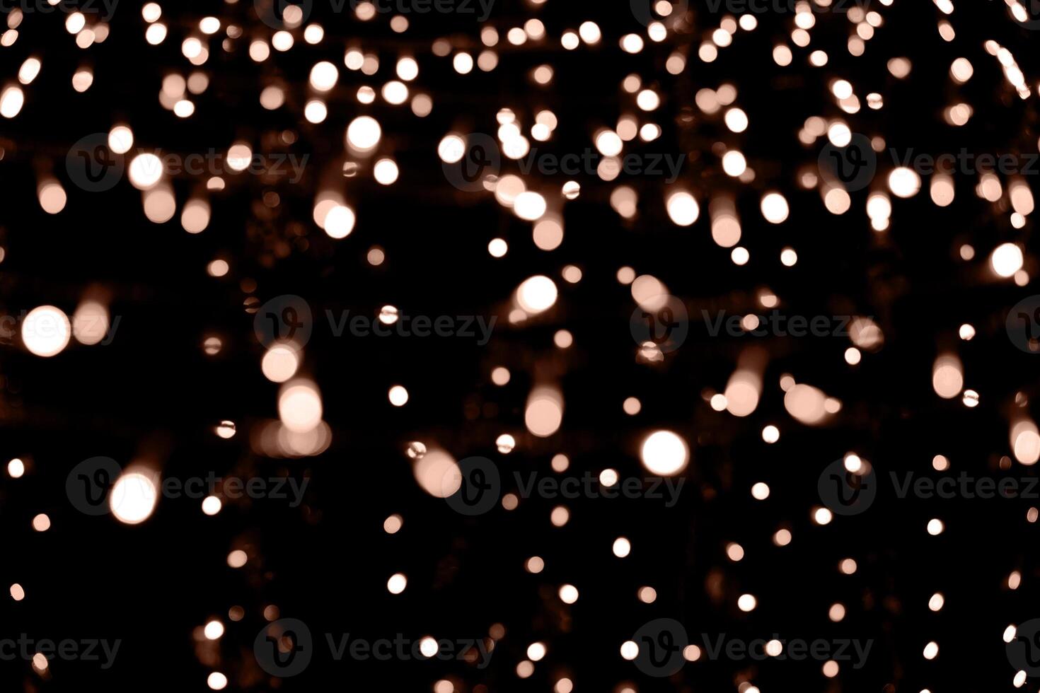 Blurry garland lights on a dark background. Festive Christmas and New Year background. Soft focus. Image toned in color of the year 2024 - Peach Fuzz photo