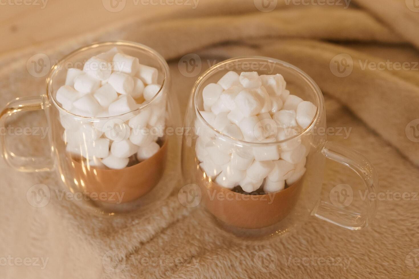 Two glass mugs of hot chocolate with marshmallows on cozy blanket. photo