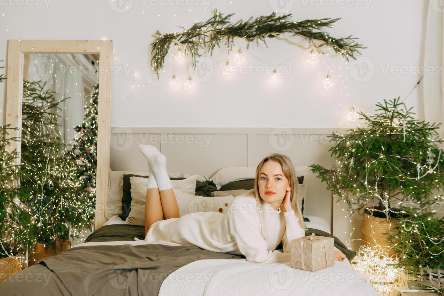 A blonde woman on a bed in a Scandinavian interior decorated for Christmas. A Christmas gift in a craft package. The period of the winter New Year holidays. photo