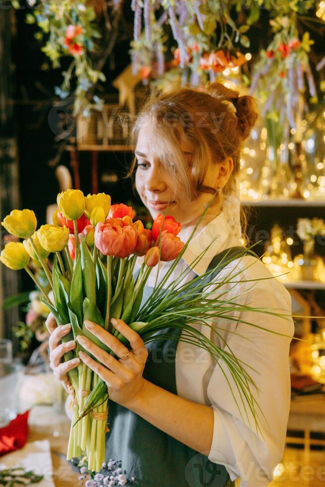 A woman in her florist shop collects bouquets of flowers. The concept of a small business. Bouquets of tulips for the holiday on March 8. photo