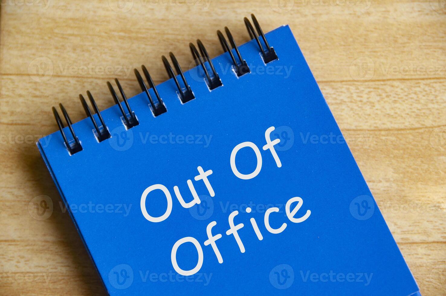 Top view of Out Of Office text on blue notepad on wooden desk. Away from work concept photo