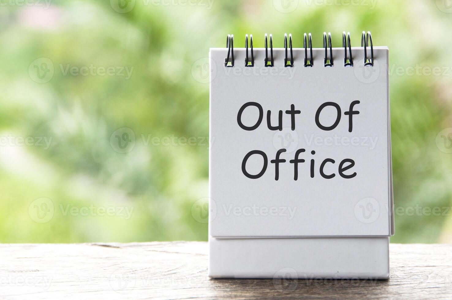 Out Of Office text on white notepad with blurred nature background photo