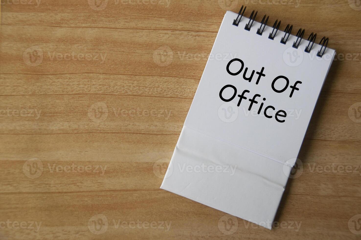 Top view of Out Of Office text on white notepad on wooden desk. Away from work concept photo