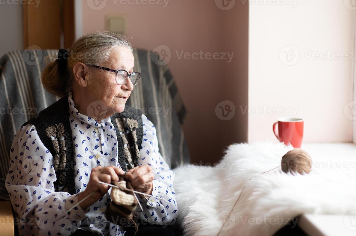 Senior woman wearing eyeglasses knitting in a nursing home by the window photo