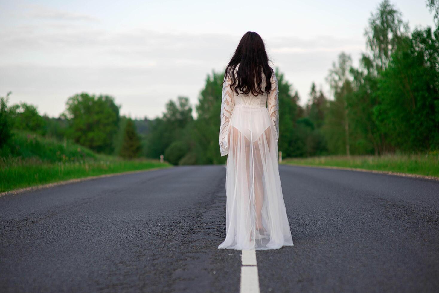 Rear view of a young woman in a white sexy dress standing on empty asphalt country road line photo
