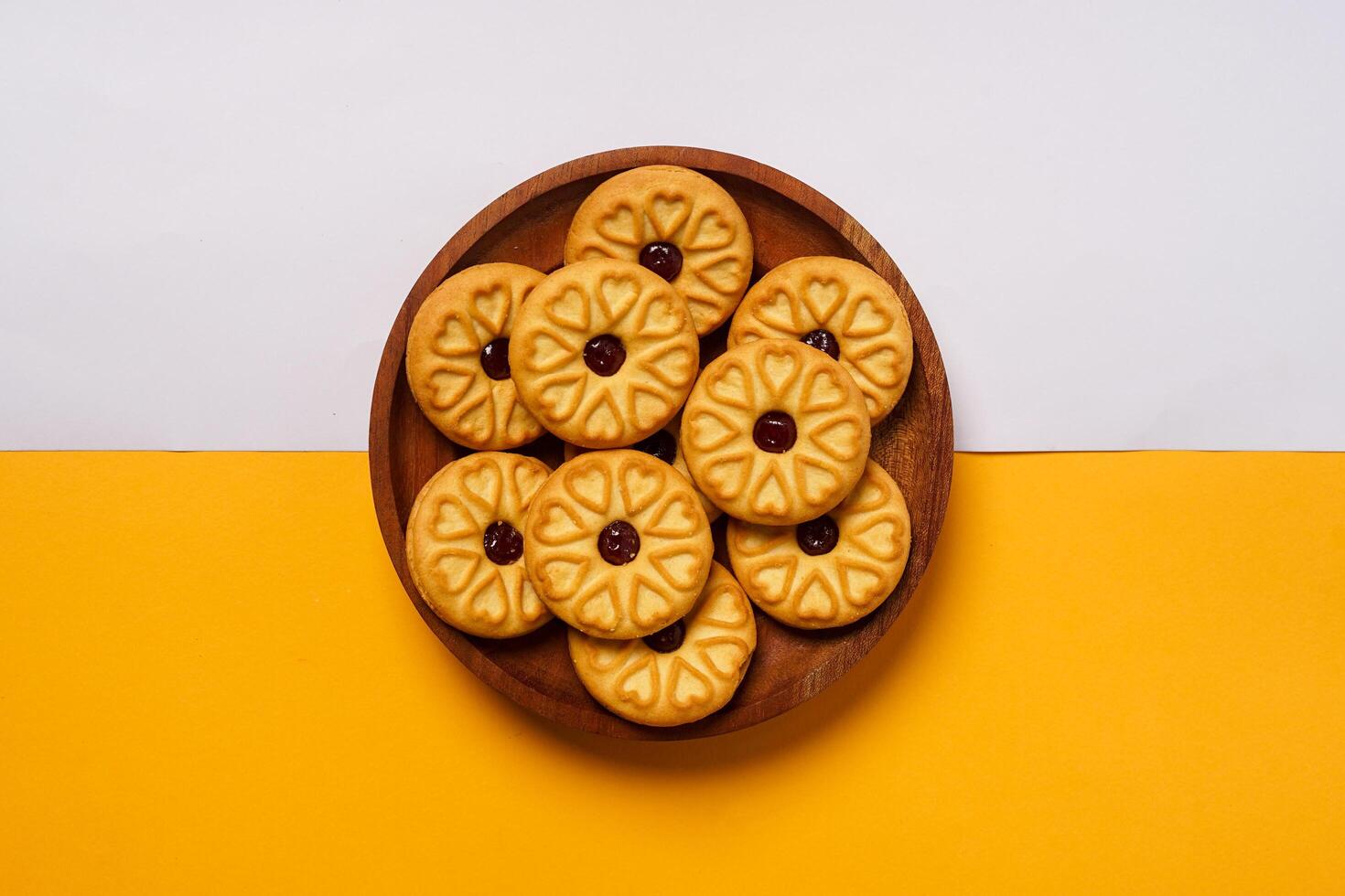 Strawberry jam biscuits on a wooden plate, decorated with a circular heart motif on their surface, isolated on white and orange background. High resolution photo. photo