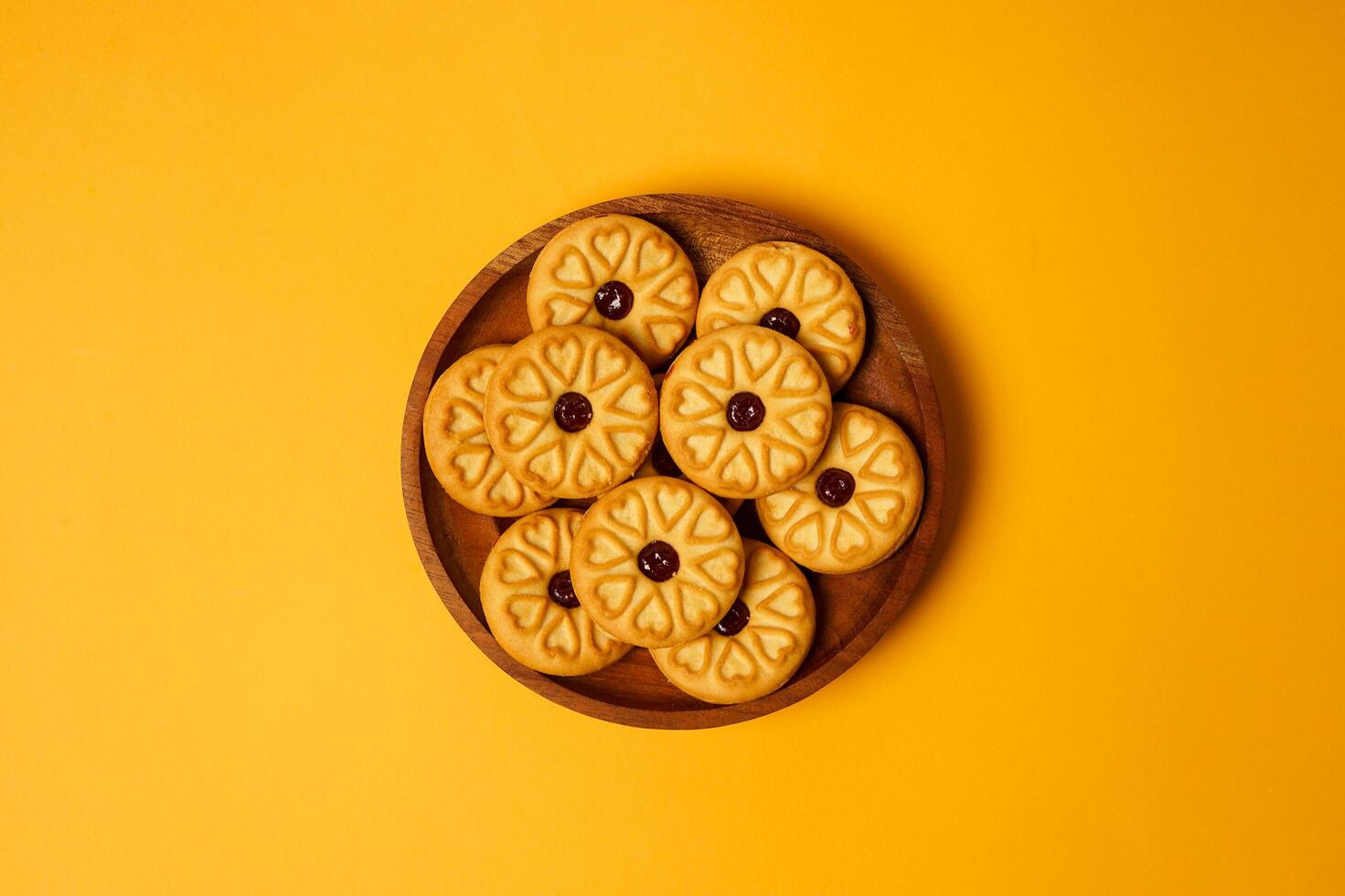 Strawberry jam biscuits on a wooden plate, decorated with a circular heart motif on their surface, isolated on orange background. High resolution photo. photo