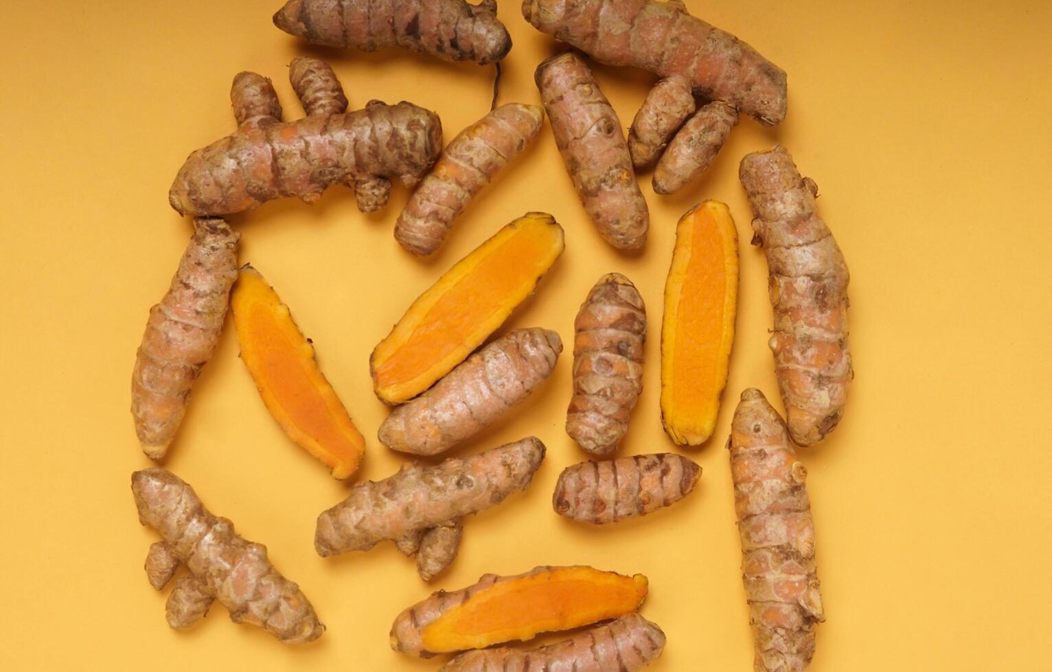 Fresh turmeric root and slices isolated on yellow background. High resolution photo. photo