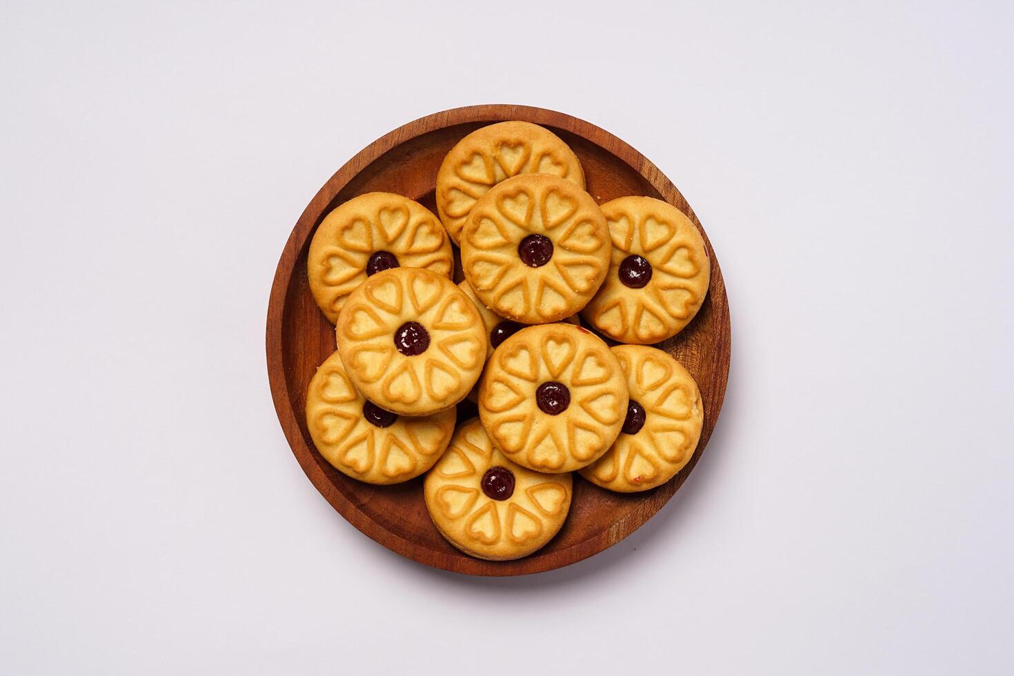 Strawberry jam biscuits on a wooden plate, decorated with a circular heart motif on their surface, isolated on white background. High resolution photo. photo