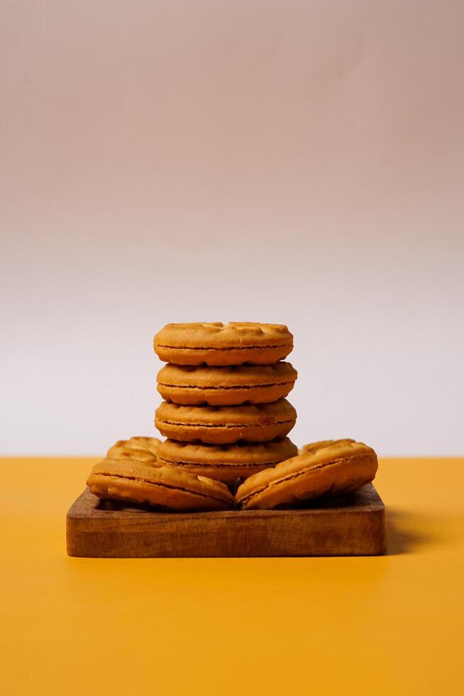 Pile of strawberry jam biscuits on a wooden plate, decorated with a circular heart motif on their surface, isolated on white and orange background. High resolution photo. photo