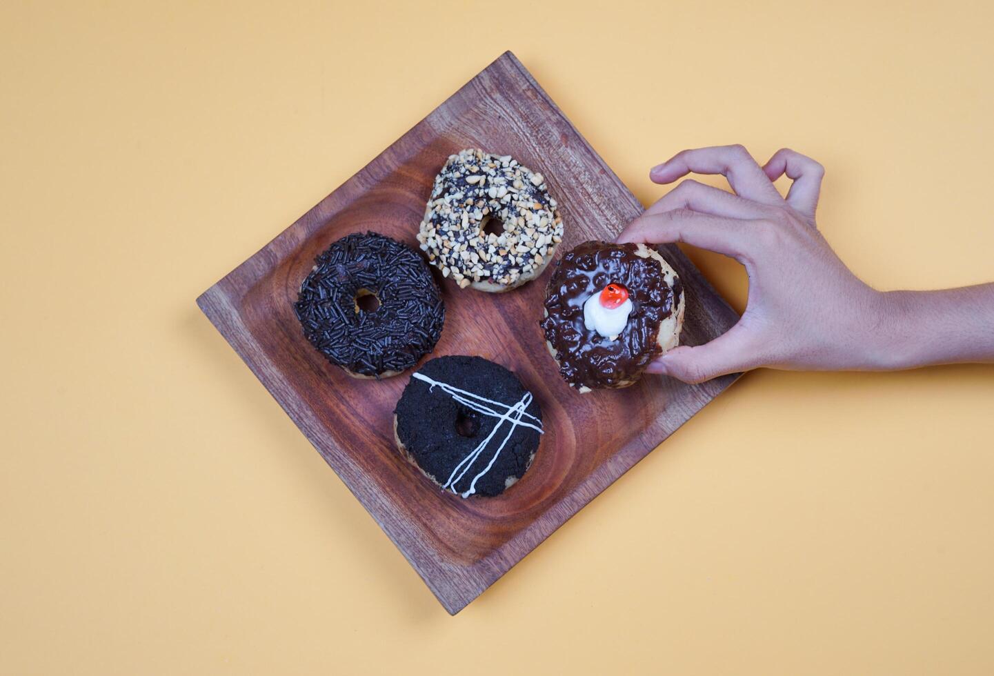 Donuts with different types of topping served on wooden plate, top view on yellow background. High resolution photo. photo