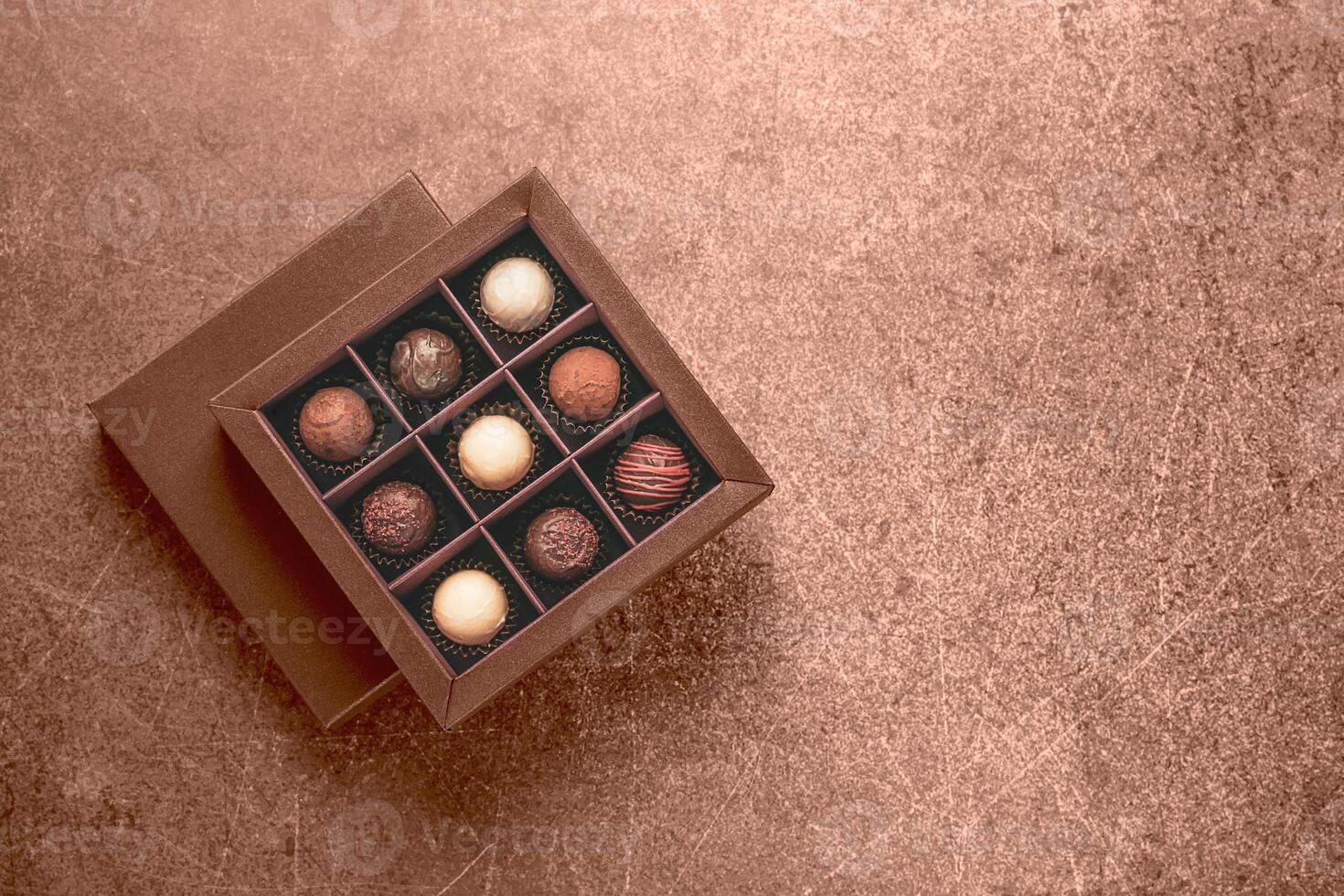 Assorted chocolate truffles in elegant brown gift box on textured surface photo