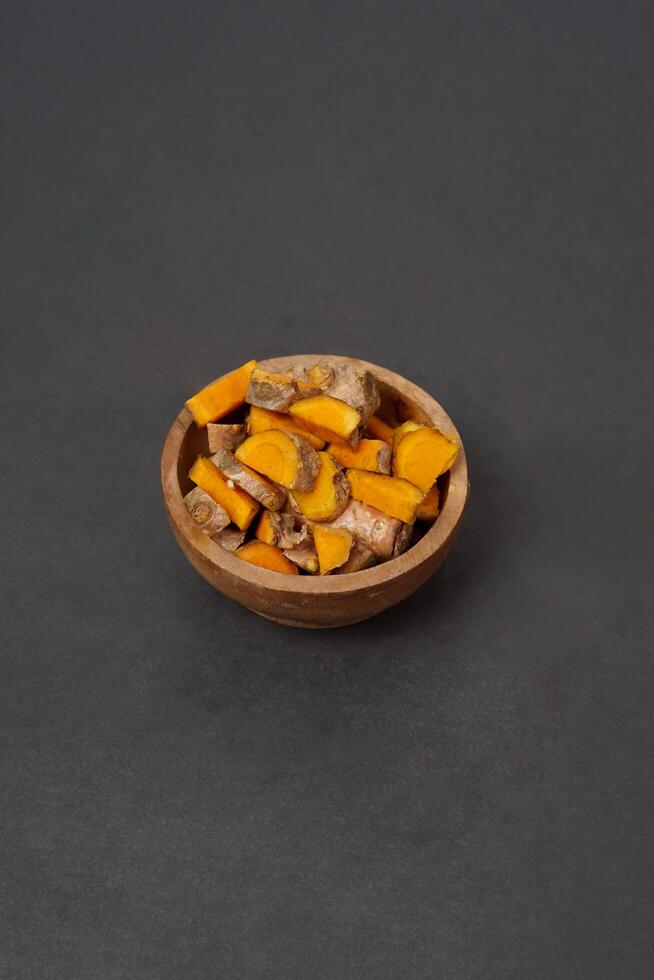 Fresh turmeric root and slices on wooden plate isolated on black background. High resolution photo. photo