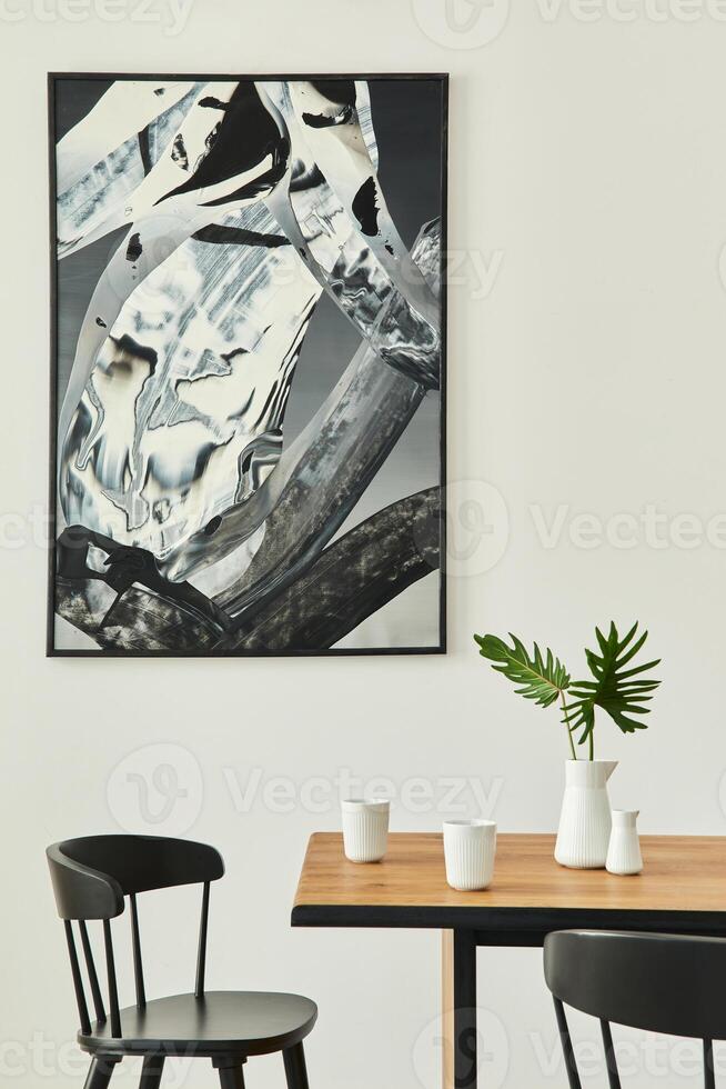 Stylish open space interior with wooden family table, black chairs, cups of coffee, tropical leaf in vase, abstract painitings on the wall and elegant accessories. Modern home decor. Template. photo