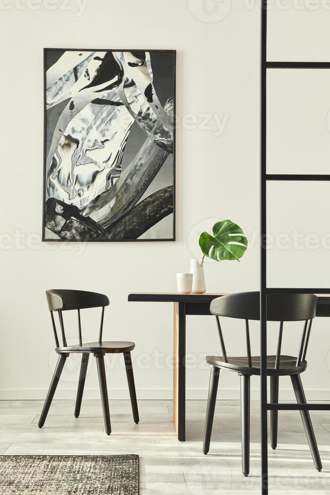Stylish open space interior with wooden family table, black chairs, cups of coffee, tropical leaf in vase, abstract painitings on the wall and elegant accessories. Modern home decor. Template. photo