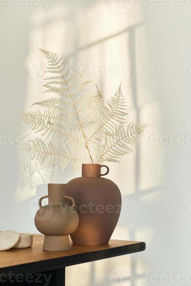 Stylish composition on the wooden table with design vases with dried flowers. Beautiful shadows on the wall. Abstract concept in modern interior. Template. photo