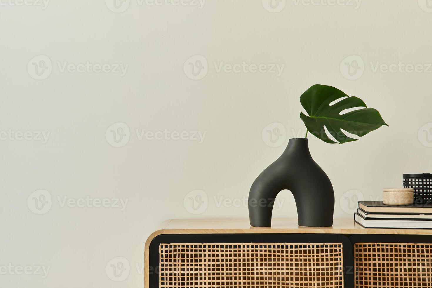 Modern scandinavian home interior with design wooden commode, tropical leaf in vase, books and personal accessories in stylish home decor. Template. Copy space. White walls. photo