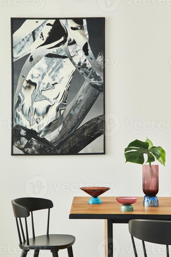 Stylish open space interior with wooden table, black chairs, deisgn glassy tray, tropical leaf in vase, abstract painitings on the wall and elegant accessories. Modern home decor. Template. photo