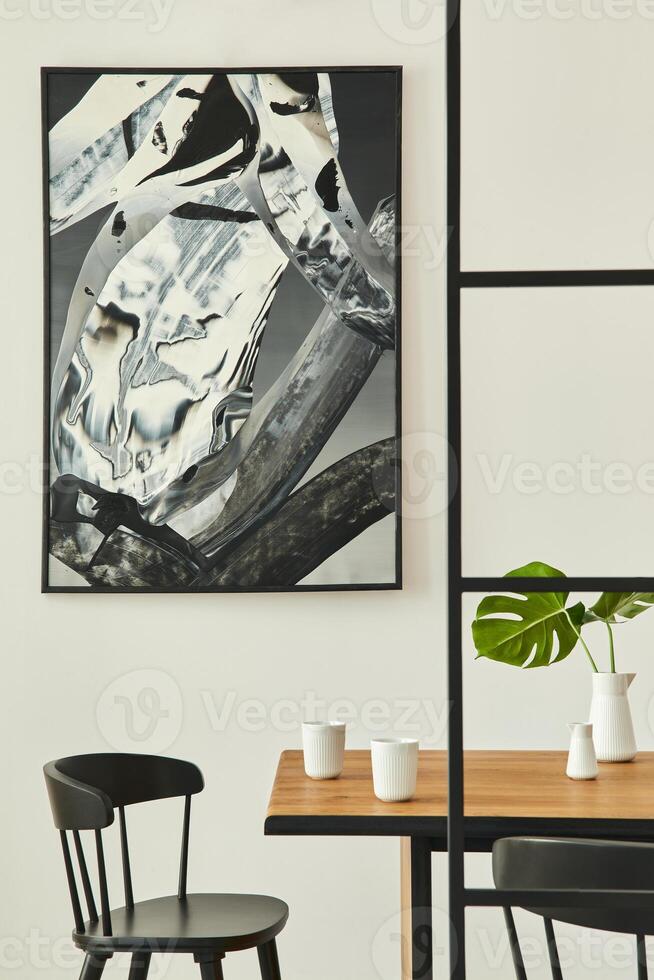 Stylish open space interior with wooden family table, black chairs, cups of coffee, tropical leaf in vase, abstract painitings on the wall and elegant accessories. Modern home decor. Template. photo