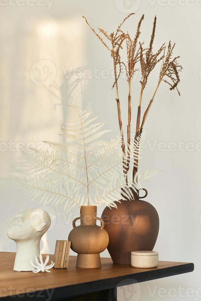 Stylish composition on the wooden table with design vases with dried flowers, book and decoration. Beautiful shadows on the wall. Abstract concept in modern interior. Template. photo