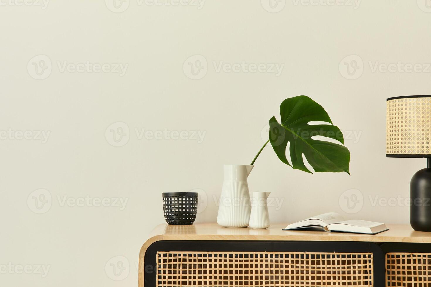 Modern scandinavian home interior with design wooden commode, tropical leaf in vase, books and personal accessories in stylish home decor. Template. Copy space. White walls. photo